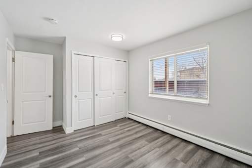 A room with a window, wooden floors, and white walls.