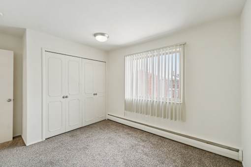 A white bedroom with a carpeted floor and a window with blinds.