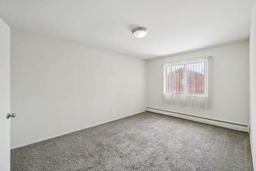 A room with a carpeted floor and a window with blinds.