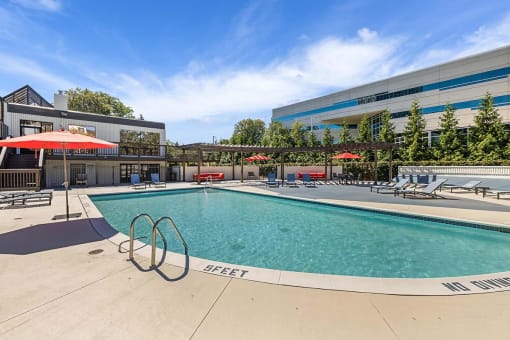 a swimming pool with chairs and umbrellas next to a building at Troy Place Apartments - Troy, MI, Troy, Michigan
