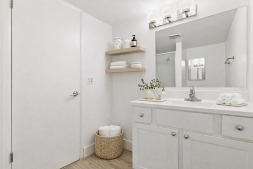 A white bathroom with a sink, mirror, and towel shelf.