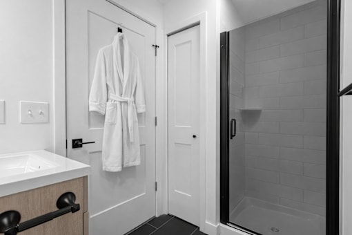 A white bathroom with a white robe hanging on the door.