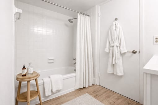 A white bathroom with a white towel hanging on the tub.