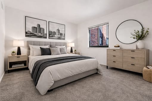 A bedroom with a large bed, a nightstand with a lamp, and a framed picture on the wall.