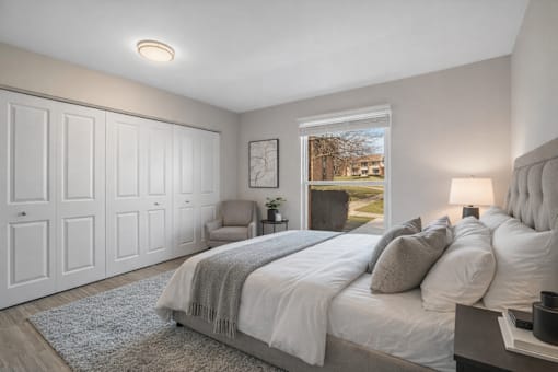 A bedroom with a large bed and a chair. at Rochester Club Apartments, Apartments, Rochester, MI
