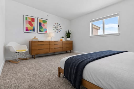 A bedroom with a bed, a chair, a dresser, and a window.