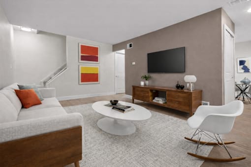 A modern living room with a white sofa, a white coffee table, a white rocking chair, a wooden cabinet, a flat screen TV, and a painting on the wall.