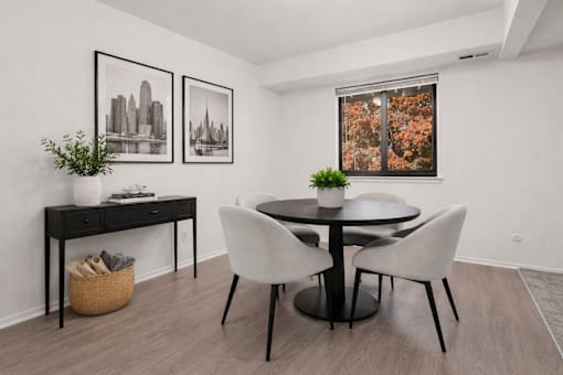 A black and white framed picture hangs on a white wall above a black desk with a plant on it.