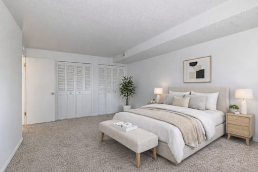 A bedroom with a large bed, a bench, and a potted plant.