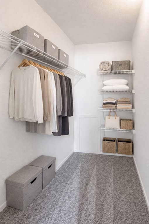 A white closet with clothes hanging and shelves with baskets and towels.