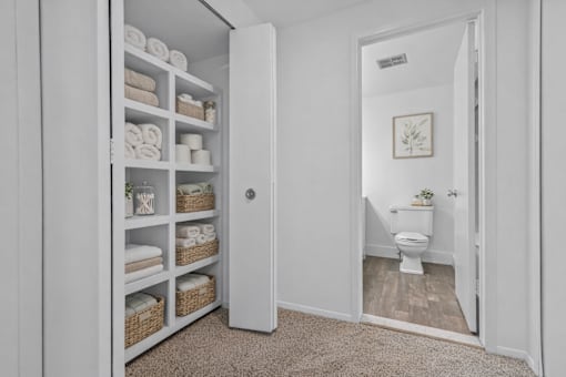 A bathroom with a toilet and a cabinet with towels and baskets.