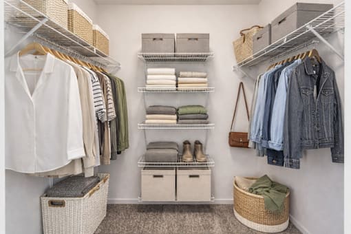 A white closet with clothes and baskets.