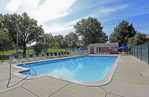 A large outdoor swimming pool surrounded by a fence and lounge chairs.