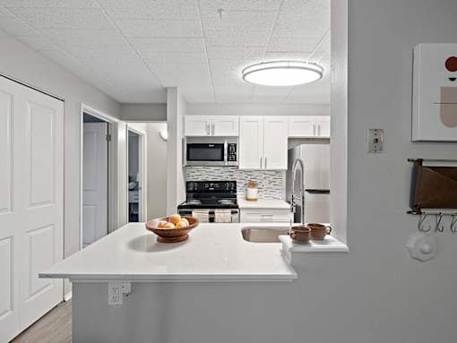 A kitchen with a white counter and a bowl of fruit on it.