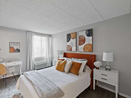 A bedroom with a bed, desk, chair, and two paintings on the wall.