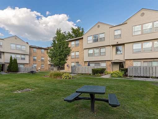A green picnic table is in the foreground of a grassy area in front of apartment buildings.