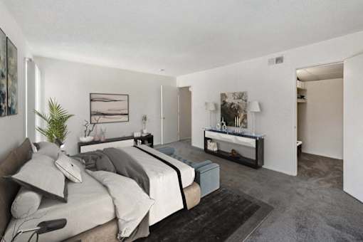 A bedroom with a bed, nightstand, and a plant at The Waverly on the Lake - Belleville, MI Apartment , Belleville, Michigan