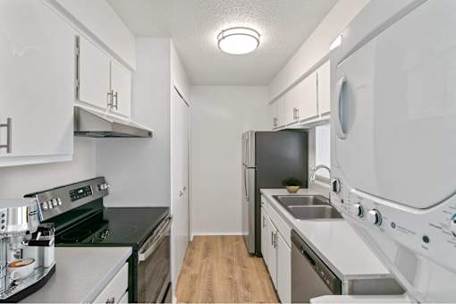 A small, white kitchen with a black stove top oven and a black dishwasher at The Waverly on the Lake - Belleville, MI Apartment , Michigan