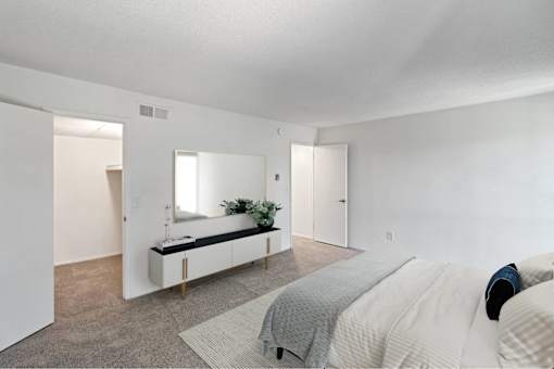 A bedroom with a bed, a mirror, and a bench with a plant on it at The Waverly on the Lake - Belleville, MI Apartment, Belleville, MI, 95050