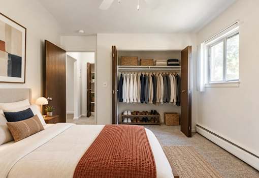A bedroom with a large bed and a closet with clothes hanging.