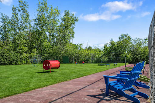 A red barrel sits on a green lawn next to a red track and blue chairs.