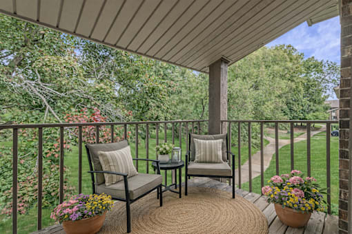 A patio with two chairs and a table with flowers on it.