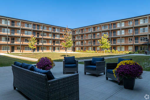 A patio area with wicker furniture and potted plants in front of apartment buildings at The Park on 13 Apartments - Royal Oak, MI Apartments, Apartments, Royal Oak, MI