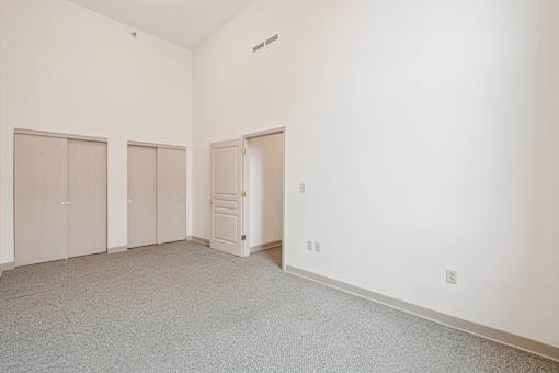 A room with white walls and carpeted floor with three closets and one door.