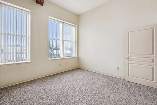 A room with a door, two windows, and a carpeted floor.