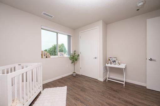 A white crib sits in a room with a wooden floor and a white table with pictures on it.