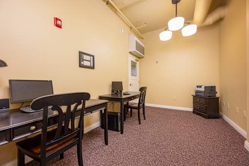 A room with a desk, chairs, and a printer.