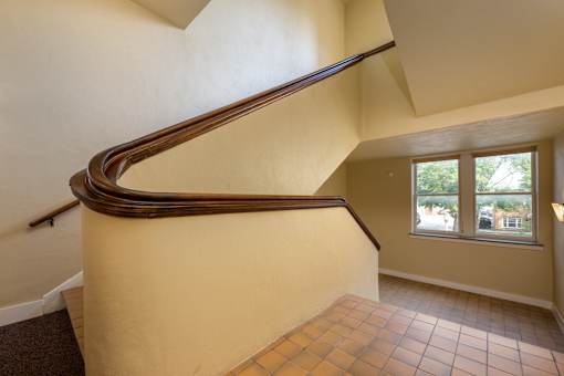 A staircase with a wooden handrail and tiled floor.