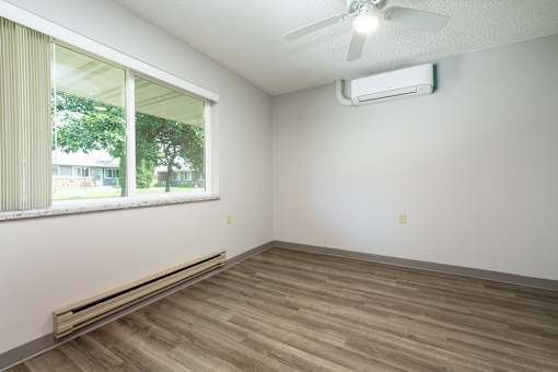 A room with a window, a ceiling fan, and a wall-mounted air conditioner.