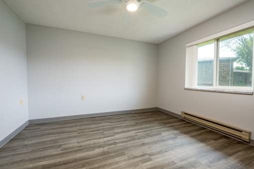 A room with a ceiling fan and a window with a view of a building and a tree.