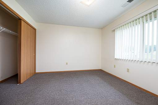 A room with a carpeted floor and a window with blinds.