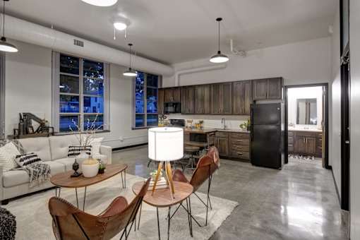 A modern kitchen and living room with a white sofa, wooden chairs, and a black refrigerator.