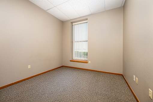 A room with a carpeted floor and a window with blinds.