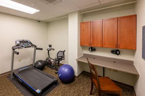 A treadmill, exercise ball, and stationary bike are in a room with a desk and cabinets.