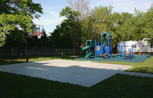 A basketball court with a basketball hoop and a playground with slides in the background.