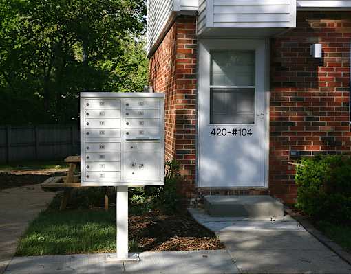 A white mailbox with the number 420-104 on it is in front of a brick house.