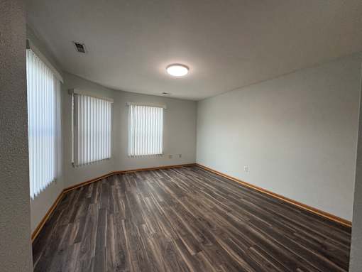 A room with wooden flooring and two windows.