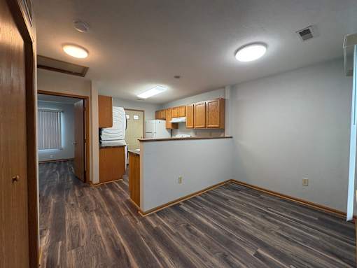 A room with wooden flooring and a kitchenette.