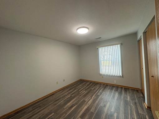 A room with wooden flooring and a window with blinds.