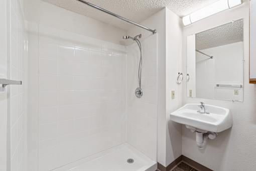 A white bathroom with a sink and a shower.