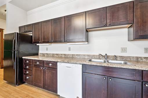 A kitchen with dark wood cabinets and a black refrigerator.