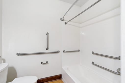 A white bathroom with a toilet, tub, and grab bars.