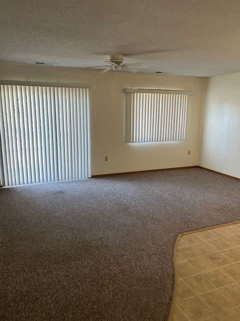 A room with a carpeted floor and a ceiling fan.