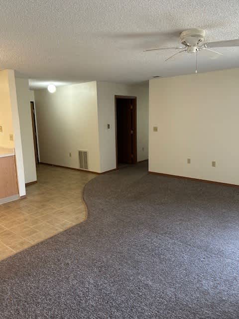 A room with a carpeted floor and a ceiling fan.