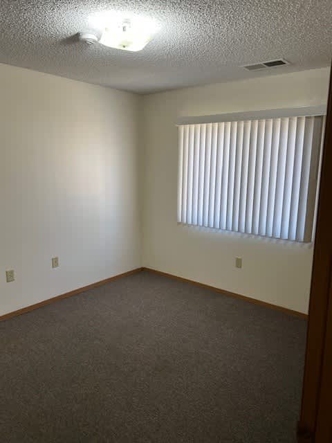A room with a carpeted floor and a window with blinds.