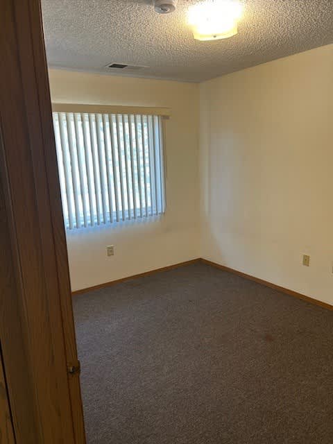 A room with a carpeted floor and a window with blinds.